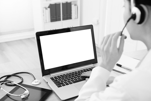 A doctor wearing a headset, adjusting her microphone, in front of her is a laptop with a white screen.