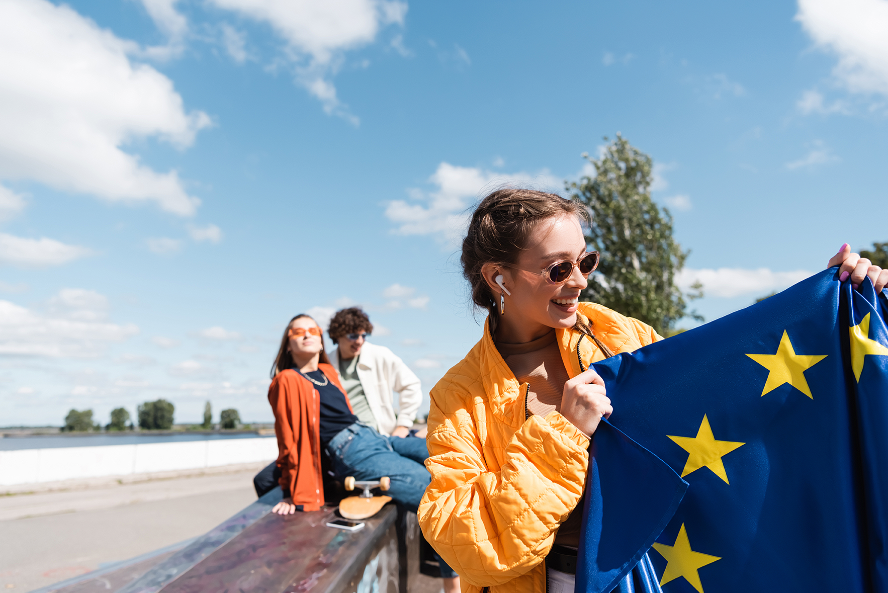 Nuori nainen pitelee Euroopan unionin lippua ulkona auringonpaisteessa, hänen takanaan on kaksi ystävää.